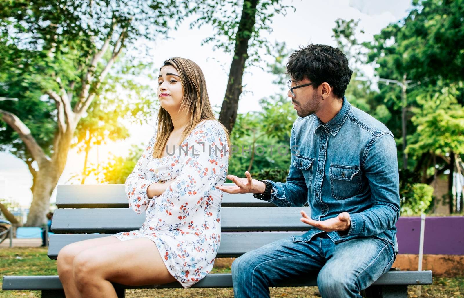 Man arguing with his girlfriend sitting in a park. Upset couple arguing in a park. A young couple arguing sitting on a park bench, Concept of couple problems and crisis