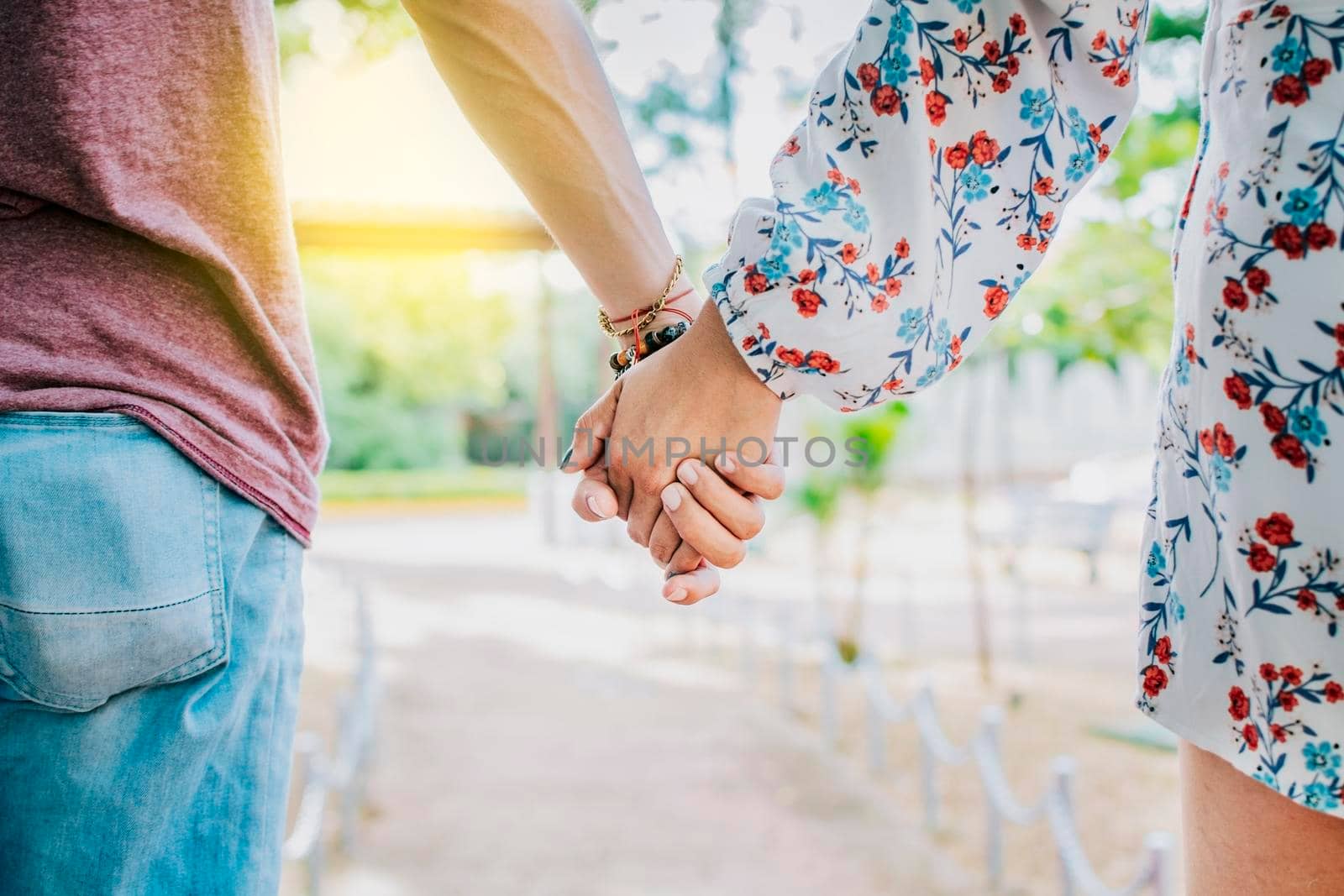 Close up of couple holding hands outdoors, Close up of young couple walking holding hands. Close-up of teenagers holding hands in a park. View of young couple holding hands outdoors by isaiphoto