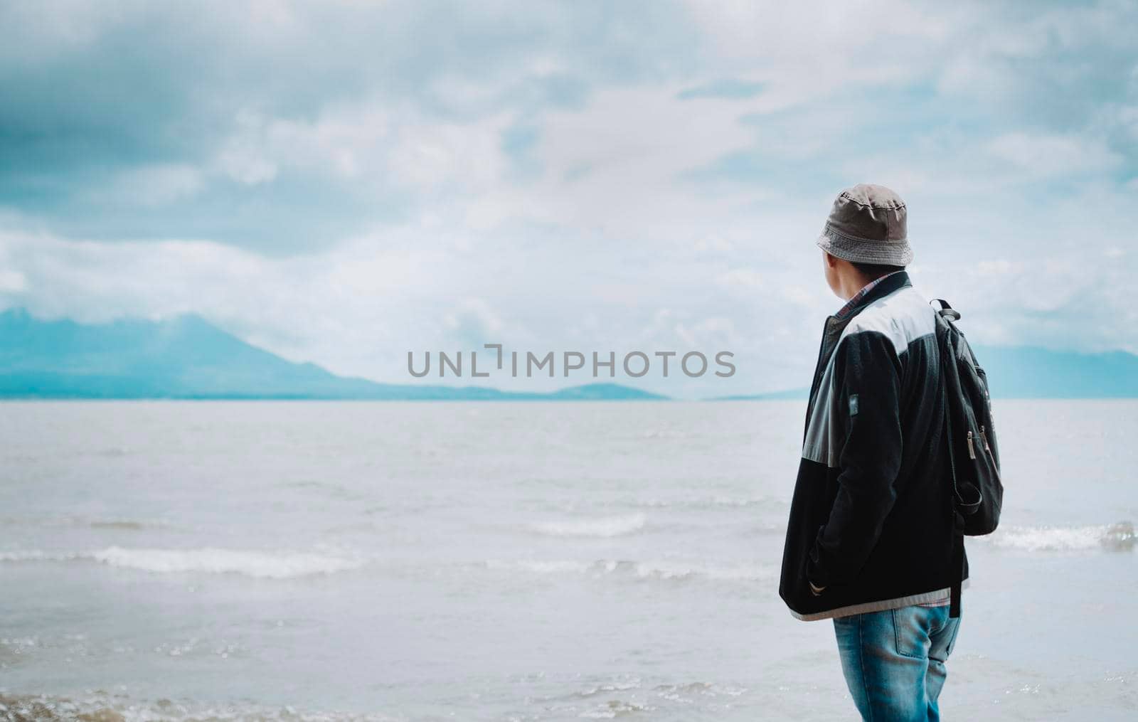 Rear view of tourist looking at a lake with volcanoes. Explorer person looking at a lake on a sunny day. Tourist man in hat from back looking at a lake with volcanoes in Rivas, Nicaragua