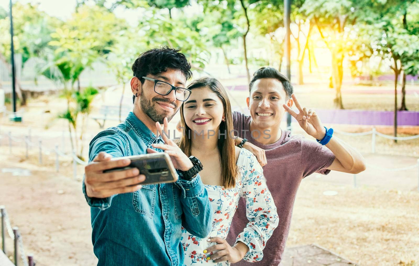 Happy friends taking a selfie in a park. Three friends standing taking a selfie in the park. Portrait of three smiling friends taking a selfie on the street. Friendship and selfie concept