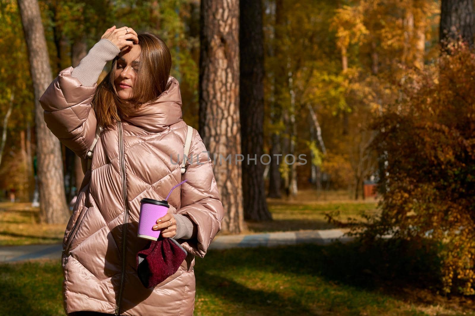 Woman in a pink jacket straightens hair with a glass of coffee tea in autumn by jovani68
