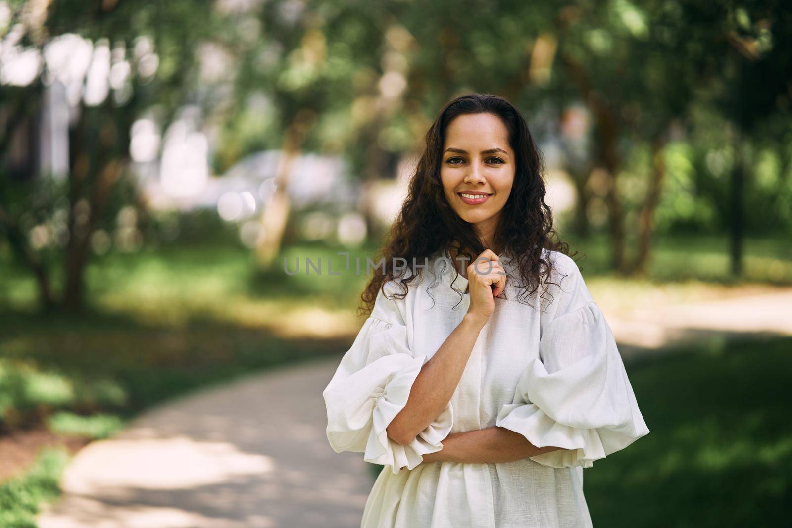 Portrait of a beautiful curly-haired brunette girl in the park. Girl smiling and holding her hair by driver-s
