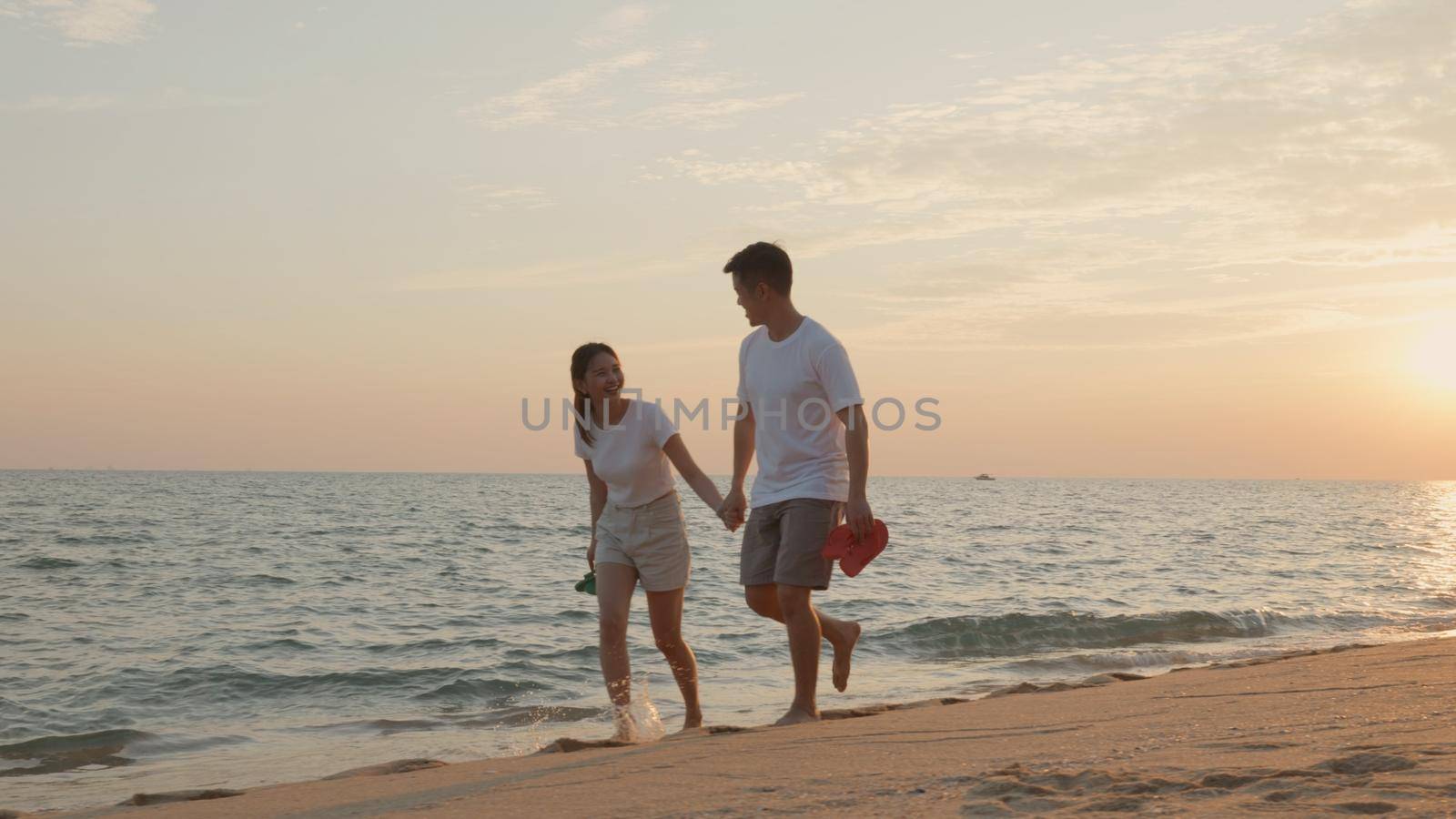 Vacation loving couple walking on beach together at sunset landscape, relaxing vacation travel summer, Asian man and woman in love holding hands walks along the sandy seashore