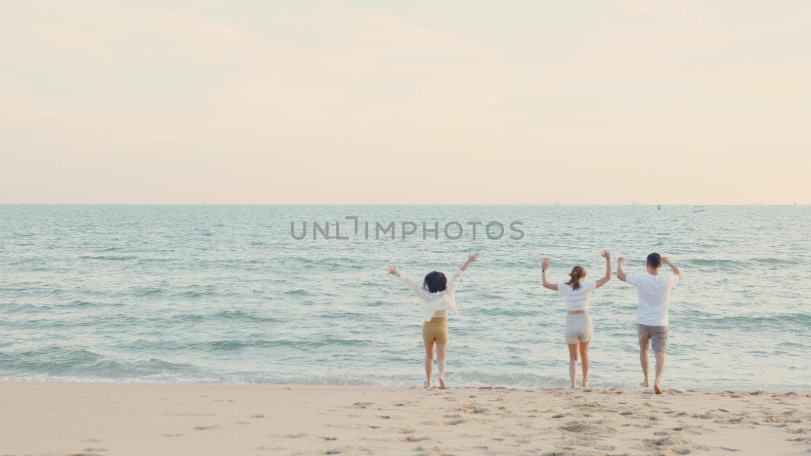 Happy friends holding hands running enjoy life funny and freedom on sand at beach together to sea by Sorapop
