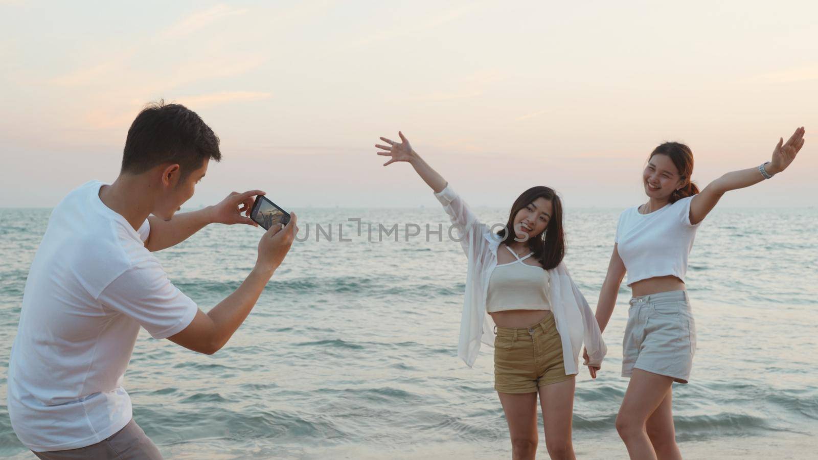 Happy friends smiling and posing taking photo from smartphone and having fun together on beach in holiday vacation time at sunset, Young Asian group woman and man in summer travel outdoor