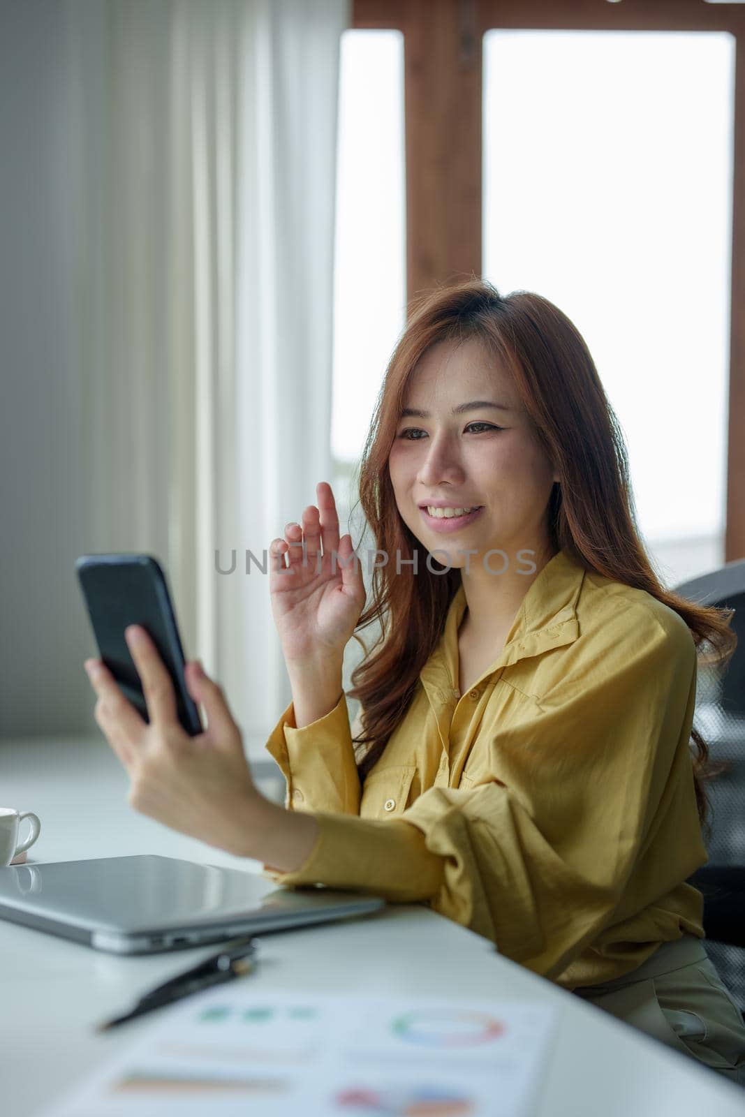 Portrait of a woman using her phone to make video calls or call a friend while taking a break at her desk by Manastrong