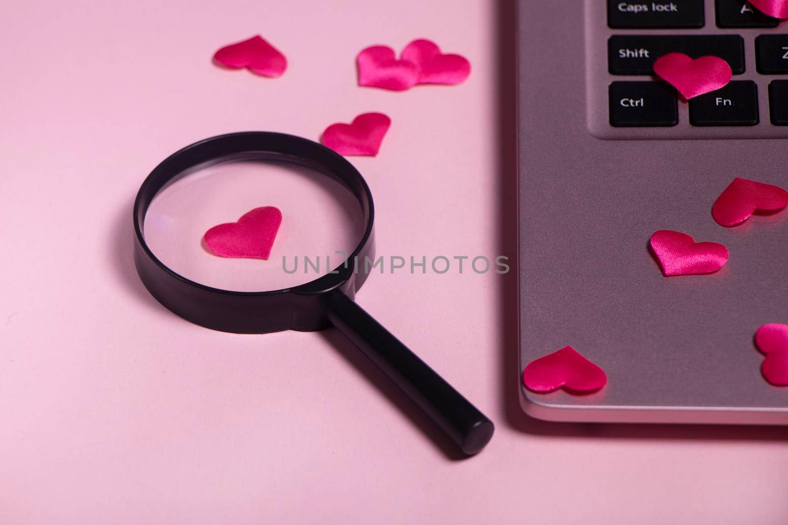 Red heart on the computer keyboard, magnifying glass with handle. Concept of searching for love on the internet, internet dating site, copyspace, place for text. Pink laptop on pink background.