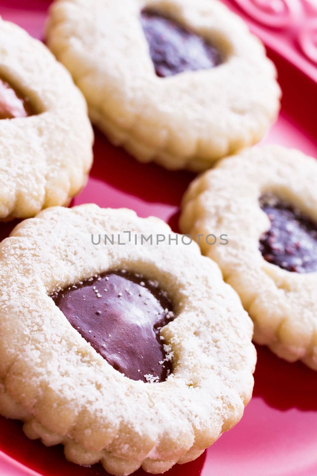 Linzer Torte cookies on red plate with powdered sugar sprinkled on top.