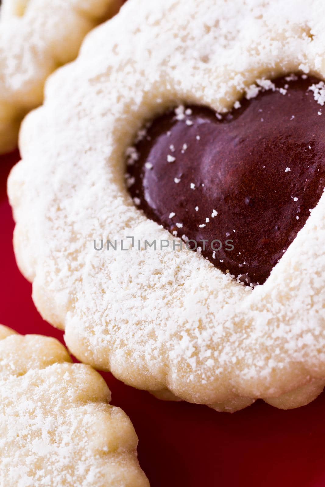 Linzer Torte cookies on red plate with powdered sugar sprinkled on top.