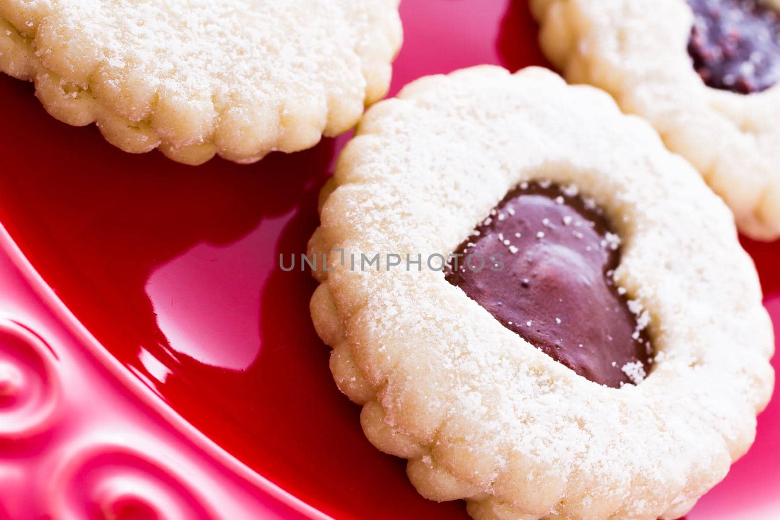 Linzer Torte cookies on red plate with powdered sugar sprinkled on top.