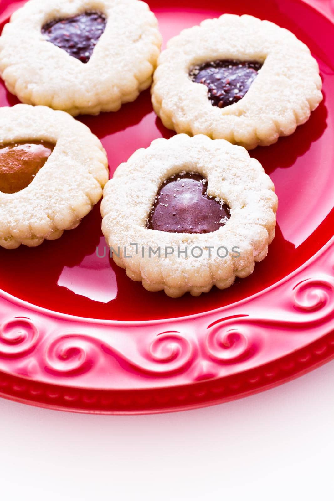 Linzer Torte cookies on red plate with powdered sugar sprinkled on top.