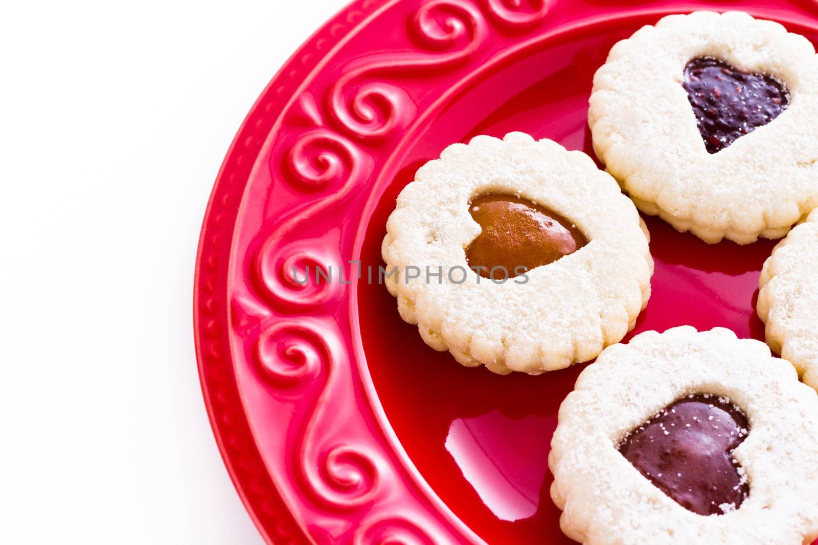 Linzer Torte cookies on red plate with powdered sugar sprinkled on top.