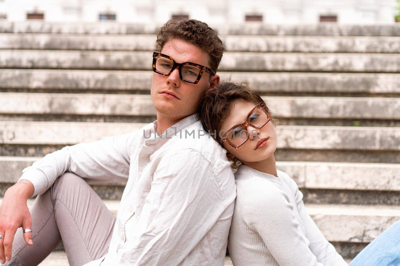 Young beautiful hipster couple in love sitting stairs on old city street, summer Europe vacation, travel, fun, happy, smiling, glasses, trendy outfit, romance, date