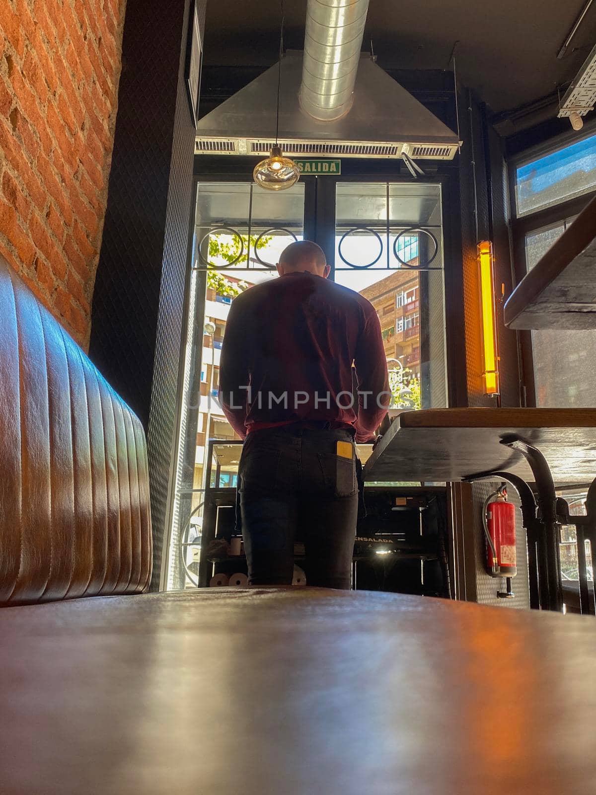 Young man standing in his restaurant entrance. Bar entrance with vintage style and light reflections. by papatonic