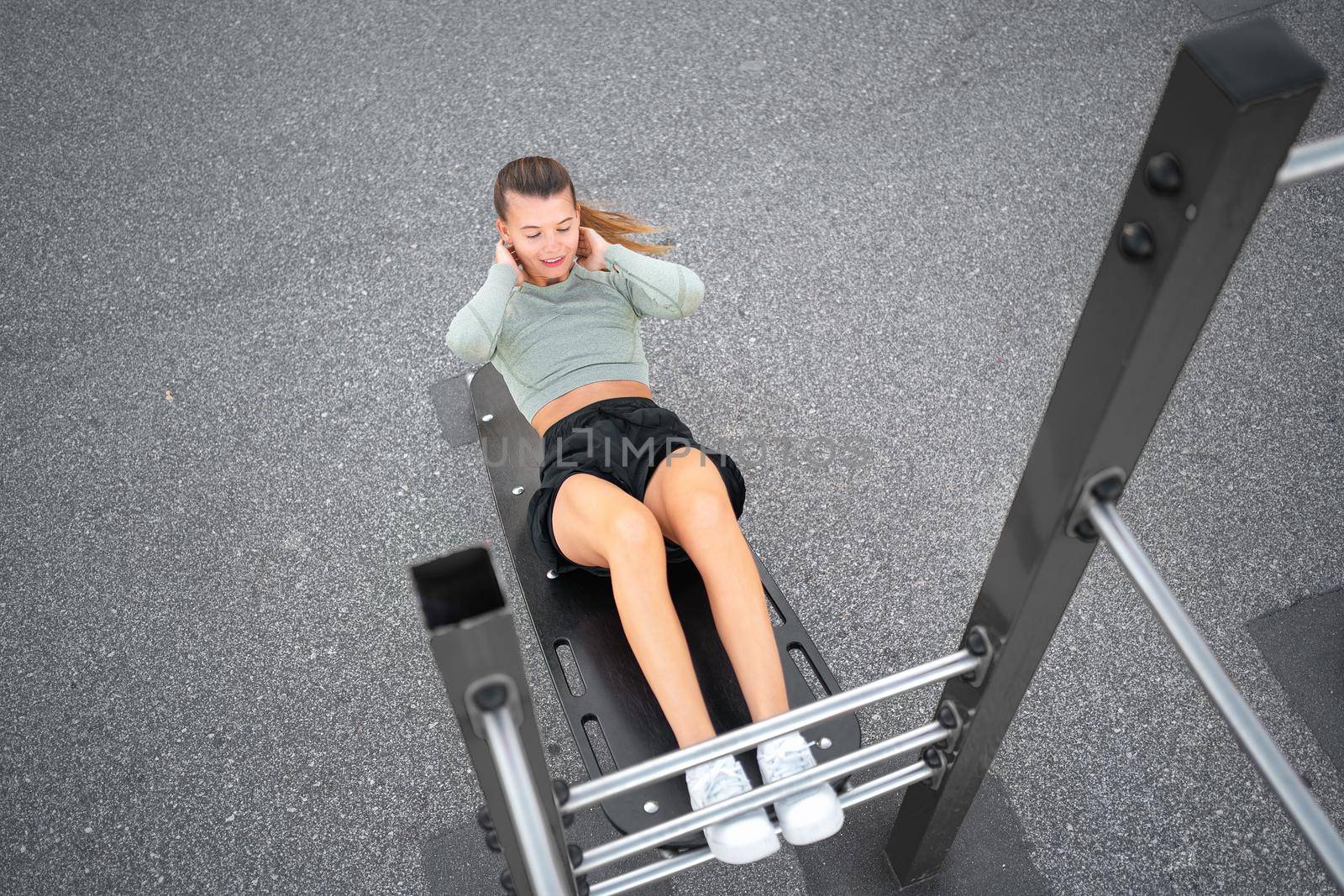 Sit-ups exercises. Active, fit sporty woman doing situps, exercising and training on fitness outdoor gym. One young, serious and athletic female exercising, working out and doing physical activity