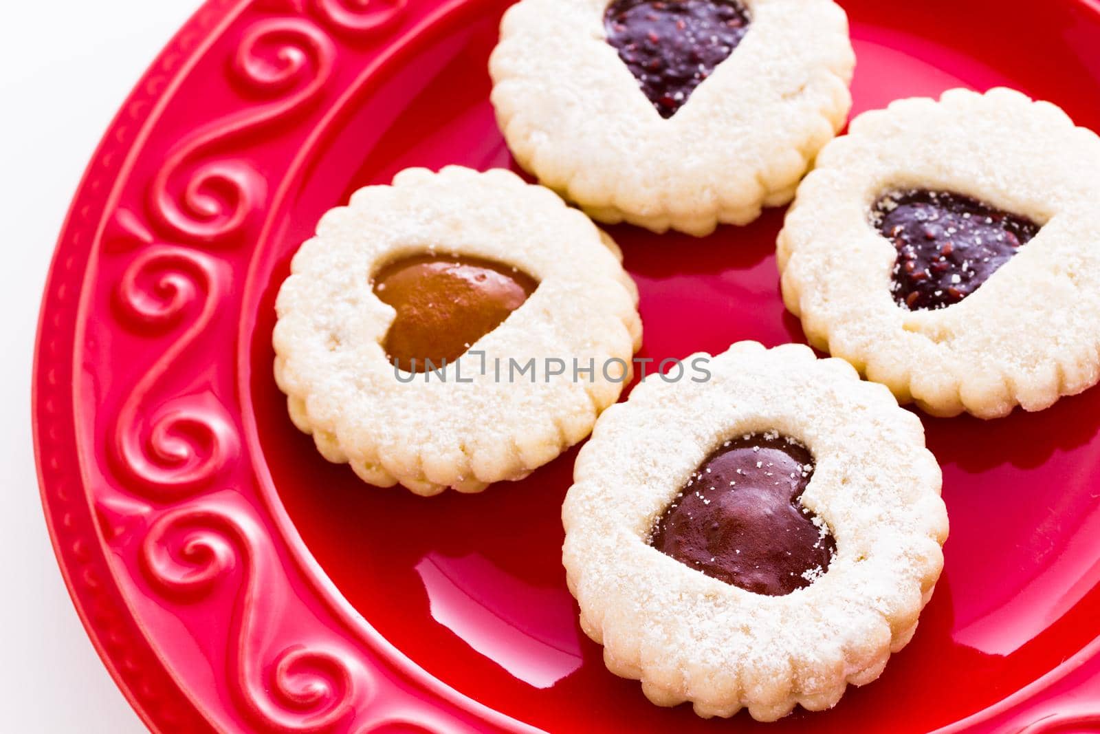 Linzer Torte cookies on red plate with powdered sugar sprinkled on top.