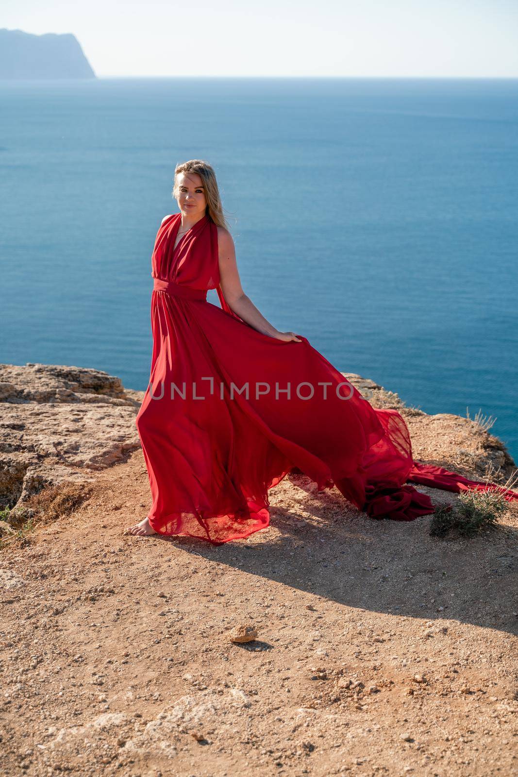 A woman in a red flying dress fluttering in the wind, against the backdrop of the sea