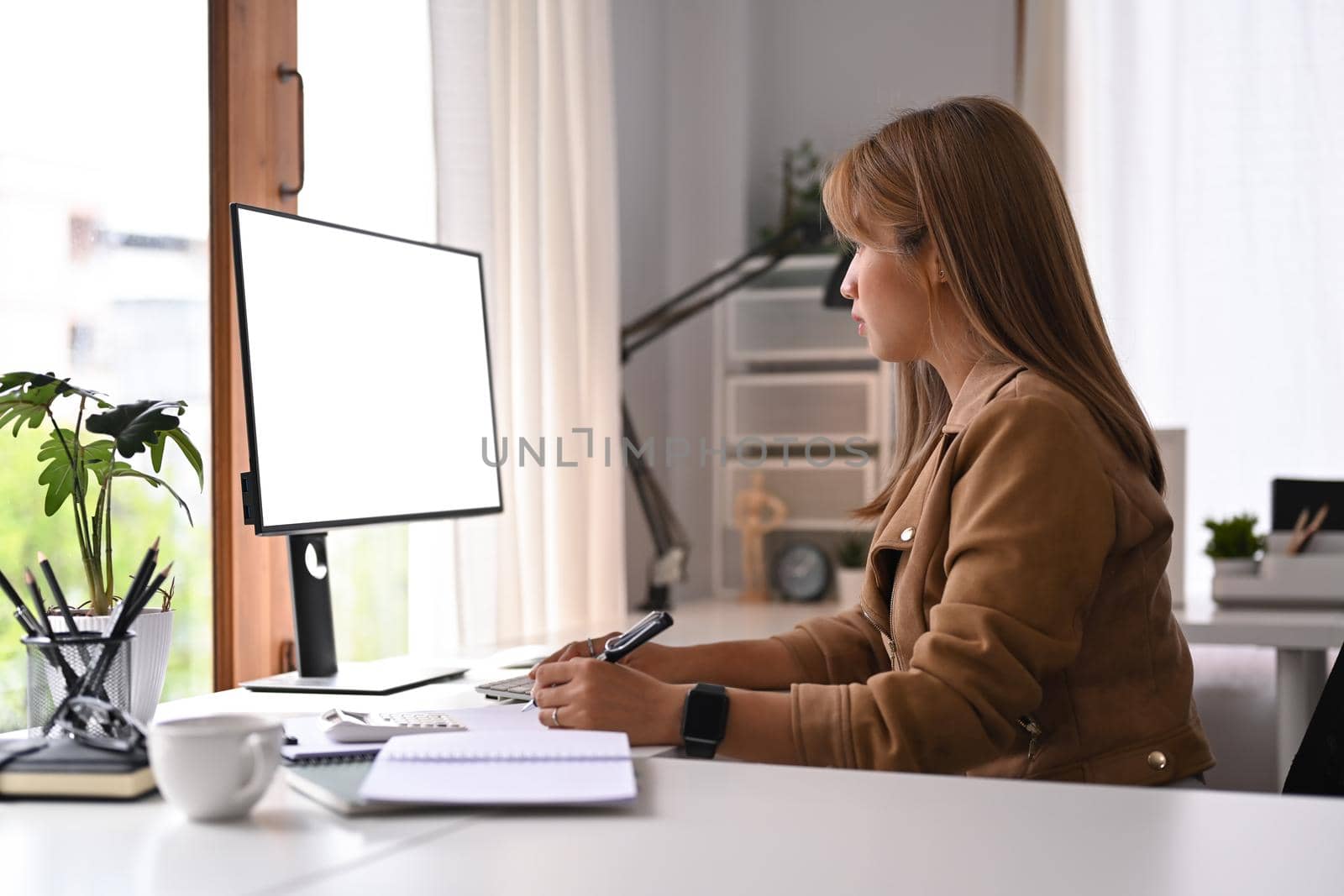 Side view of focused female entrepreneur working online with computer in her home office by prathanchorruangsak