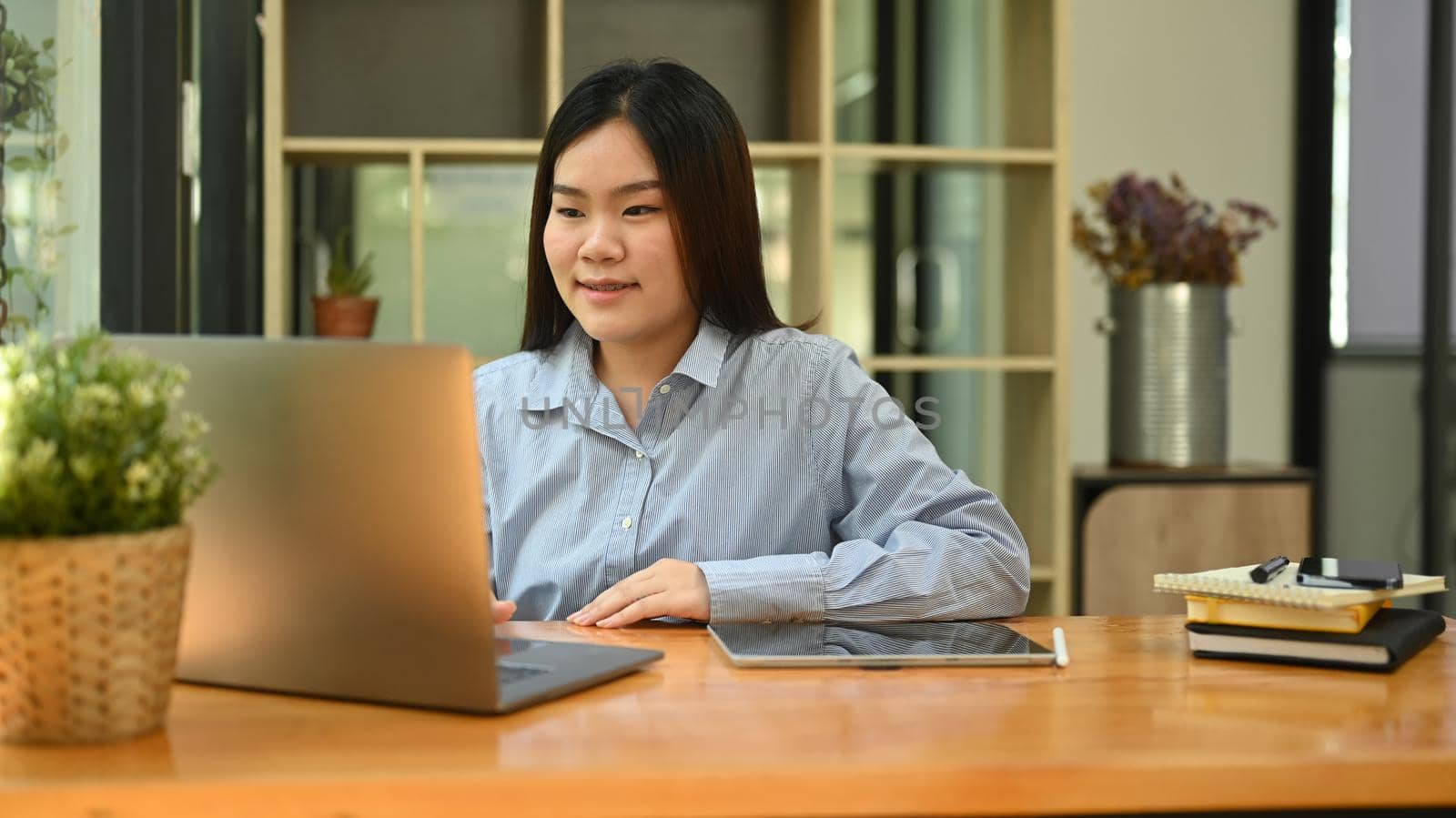 Asian woman employee checking information on laptop computer, sitting corporate office by prathanchorruangsak