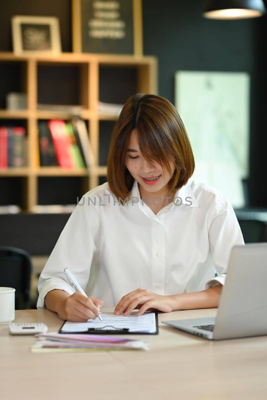 Portrait of successful entrepreneur using laptop computer and doing some paperwork at her office by prathanchorruangsak