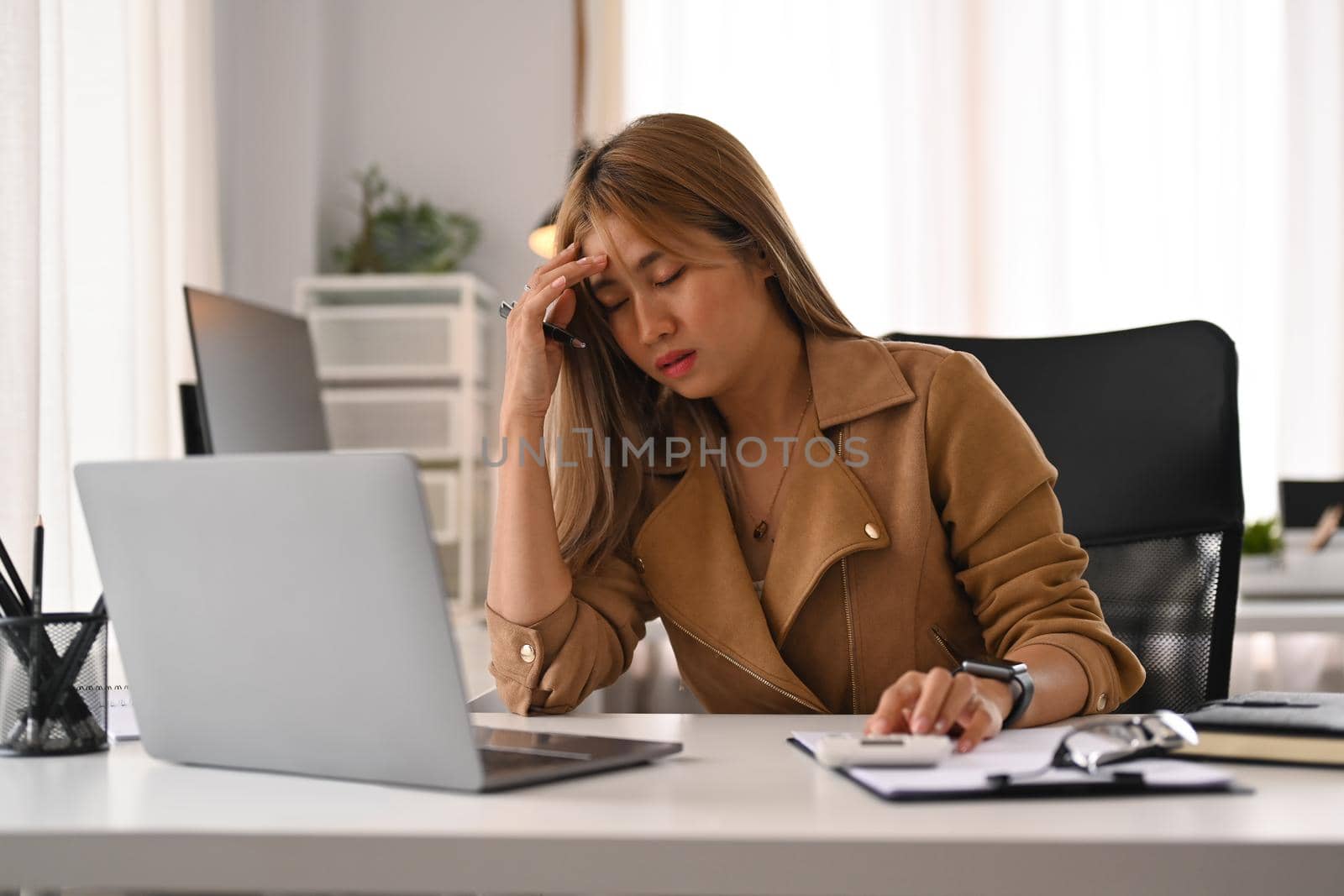 Tired businesswoman holding covering her head, feeling strong headache, exhausted from overwork or stress at work.