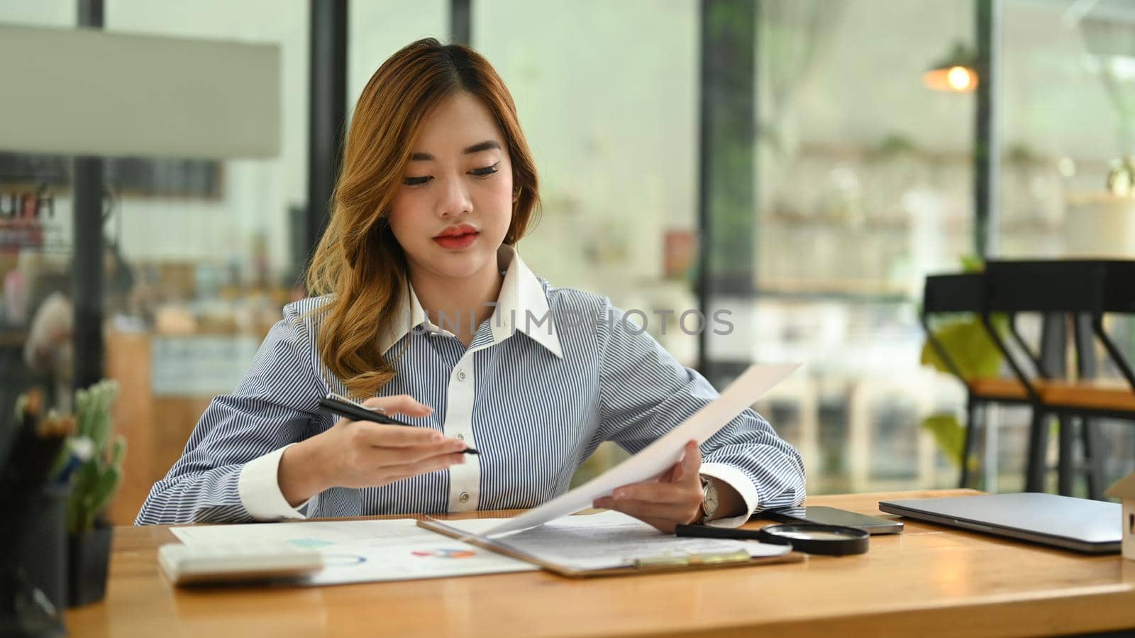 Young female accountant using calculator and examining the numerical data on financial document by prathanchorruangsak