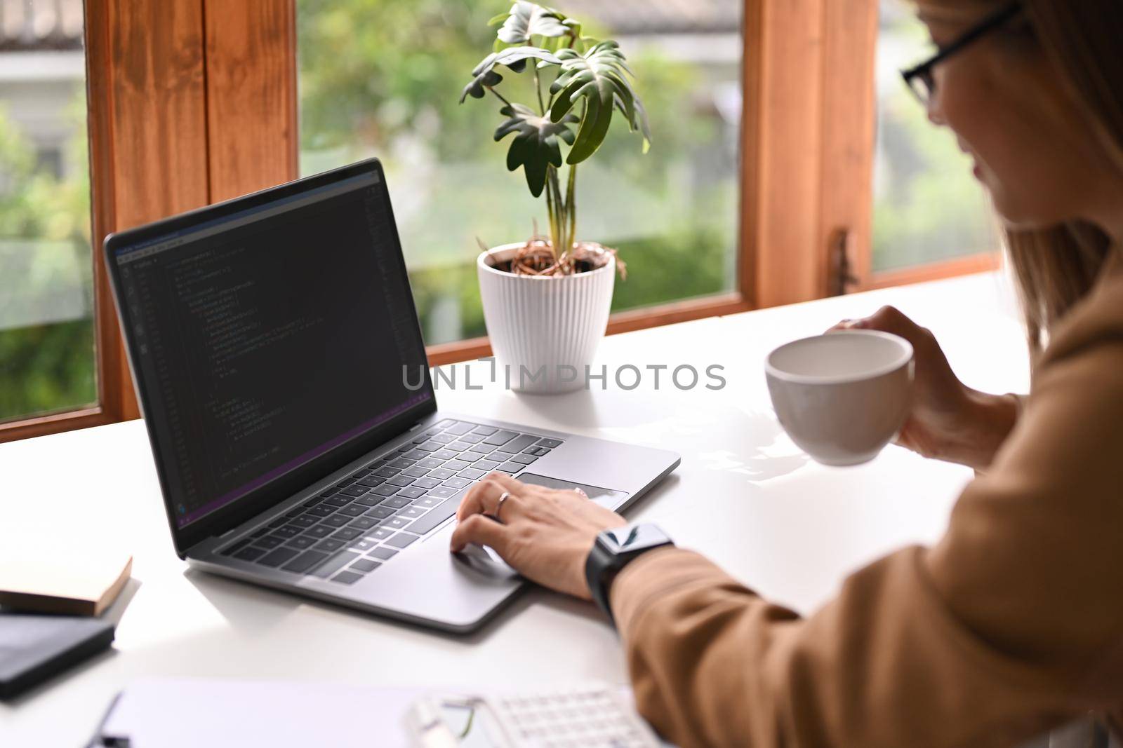 Female software developer drinking coffee and working with coded data in corporate office by prathanchorruangsak