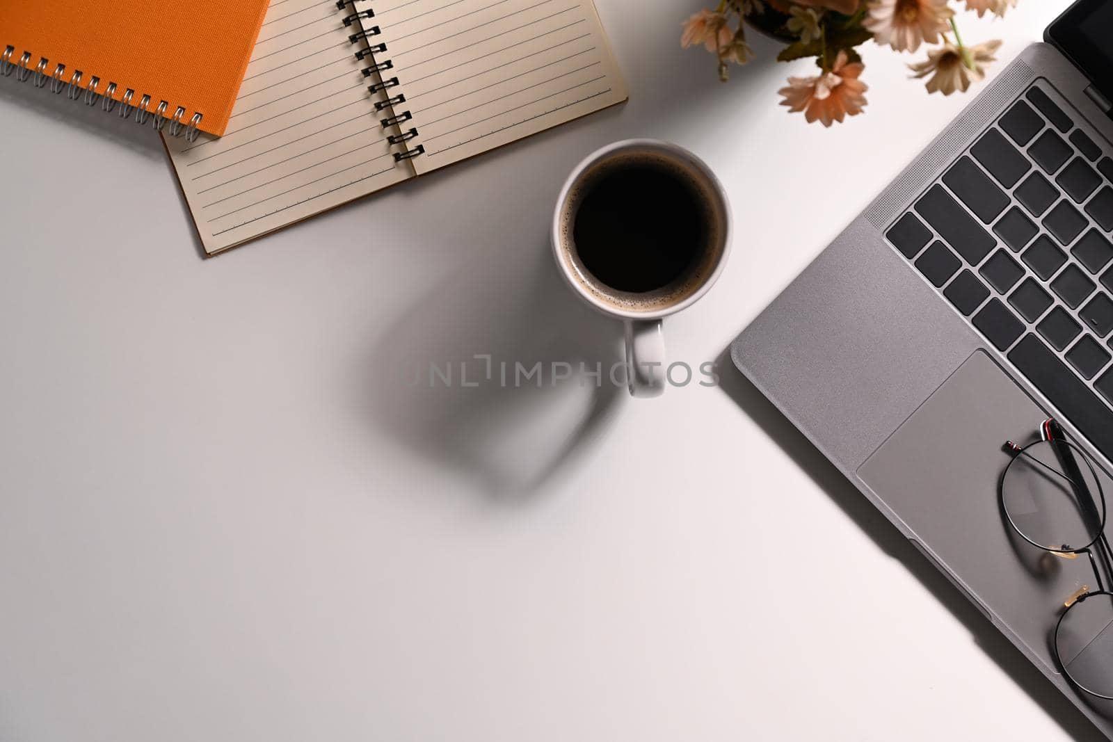 White office desk with laptop computer, cup of coffee, glasses and notebooks. Flat lay, Top view with copy space.