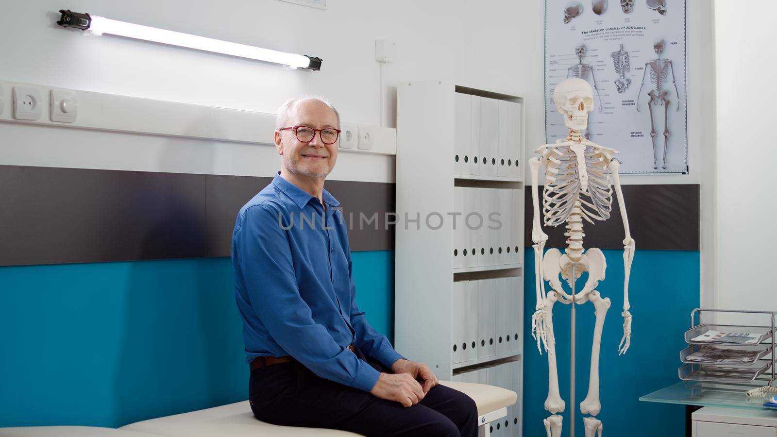 Portrait of elderly man waiting to attend checkup visit with physician in medical office, having consultation appointment at healthcare facility. Oold patient sitting in cabinet to do examination.