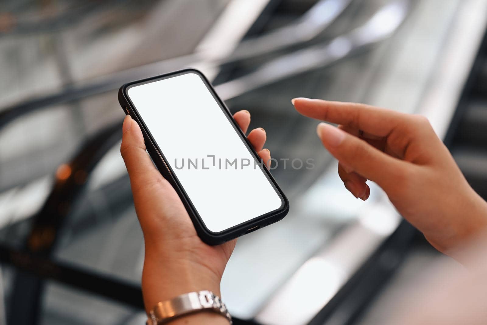 Cropped image of woman hand using smart phone with blurred escalator in background. Empty screen for your advertise text by prathanchorruangsak