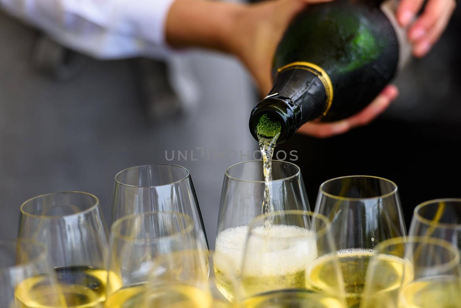 closeup of a champagne bottle pooring champagne into a champagne flute against a blurred person at a party