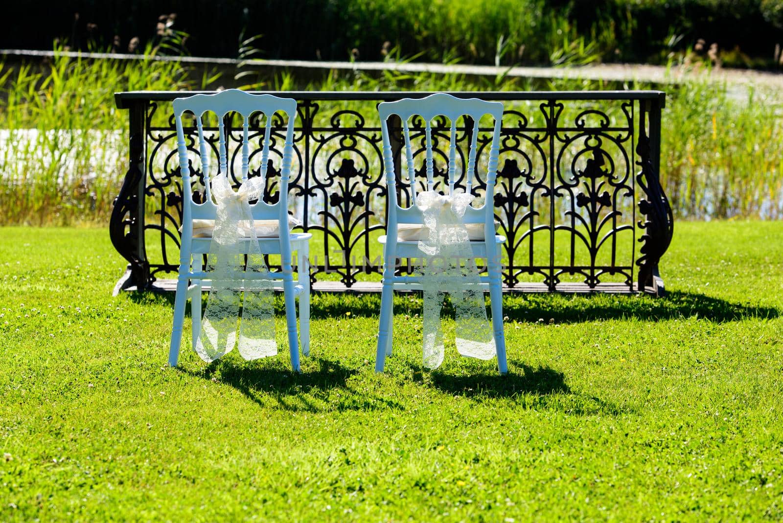 white chairs wating for people in a garden for a weddding with a lake in the background .