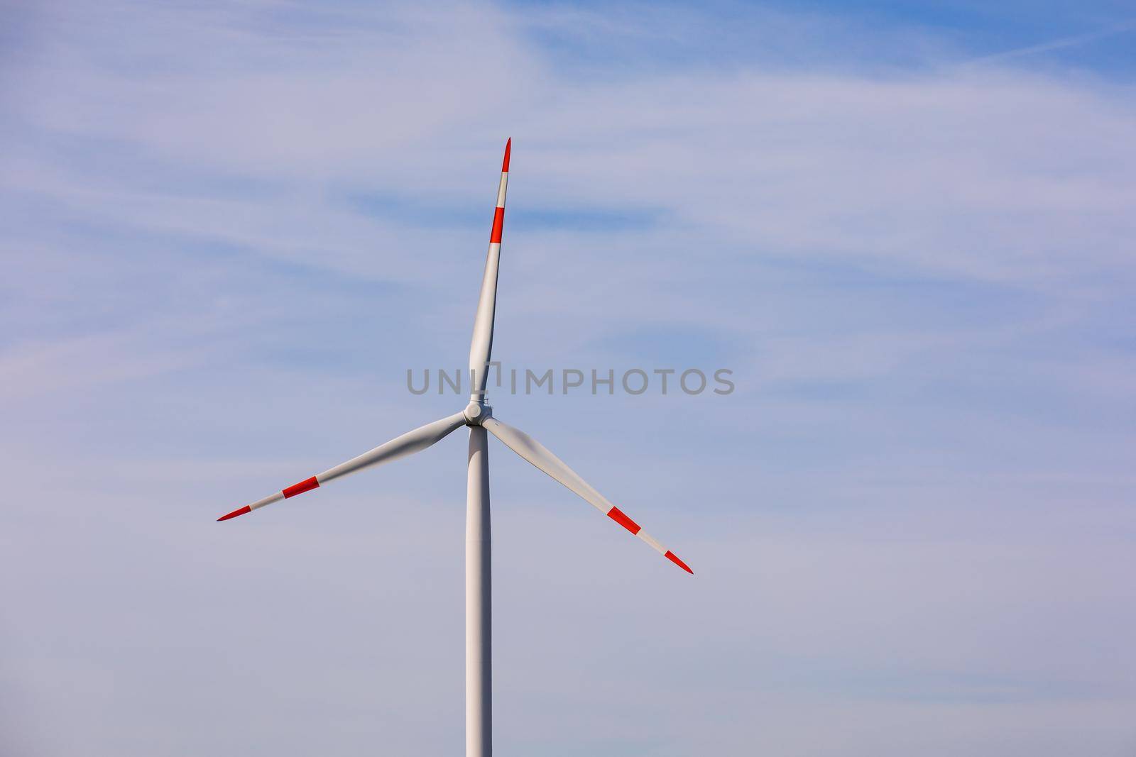 A red and white three-propeller wind turbine against the blue sky