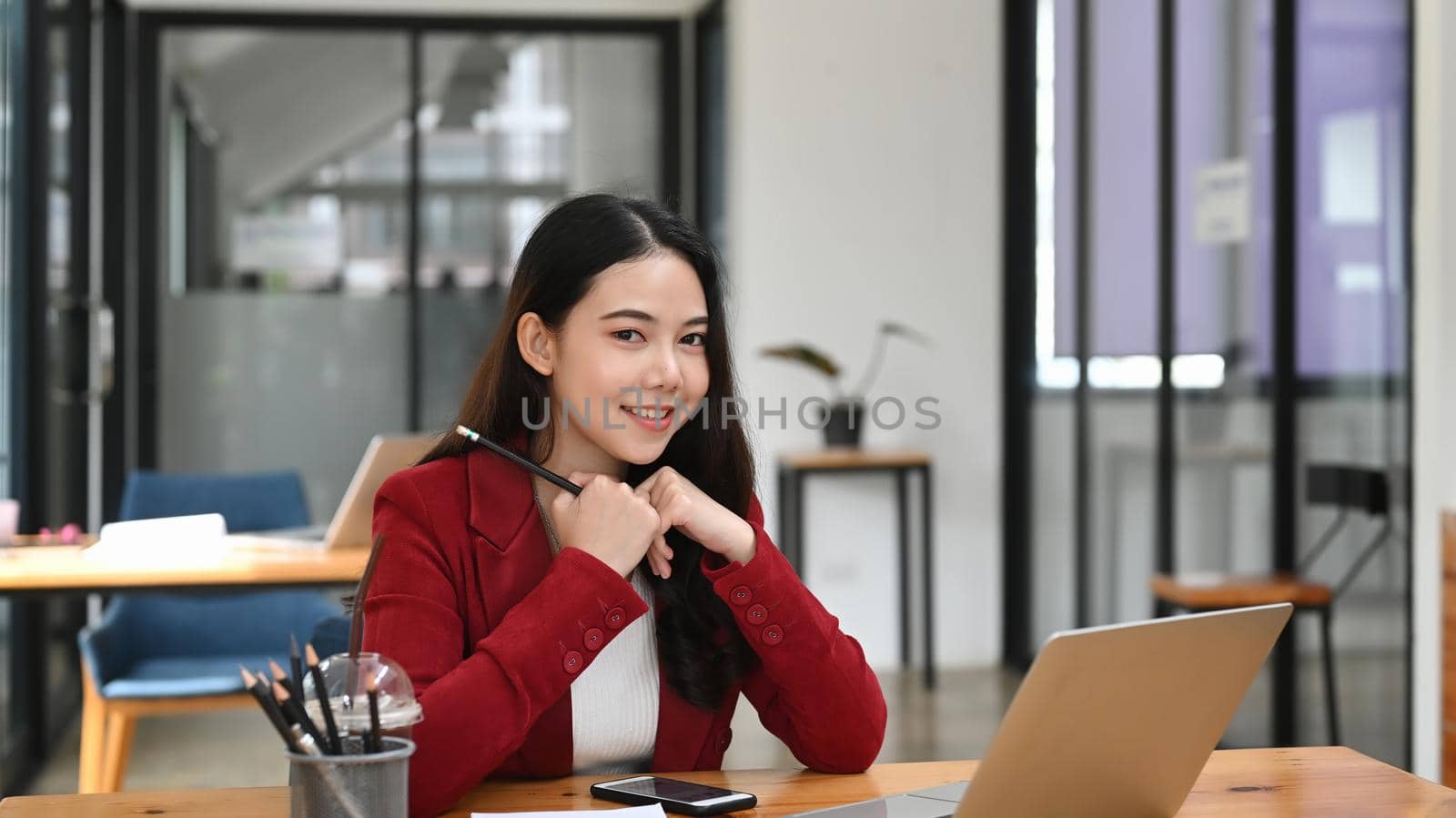 Beautiful businesswoman sitting in office and smiling to camera. by prathanchorruangsak