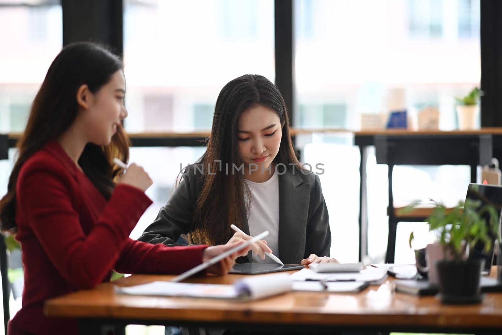 Two businesswoman colleagues working together in modern office. by prathanchorruangsak