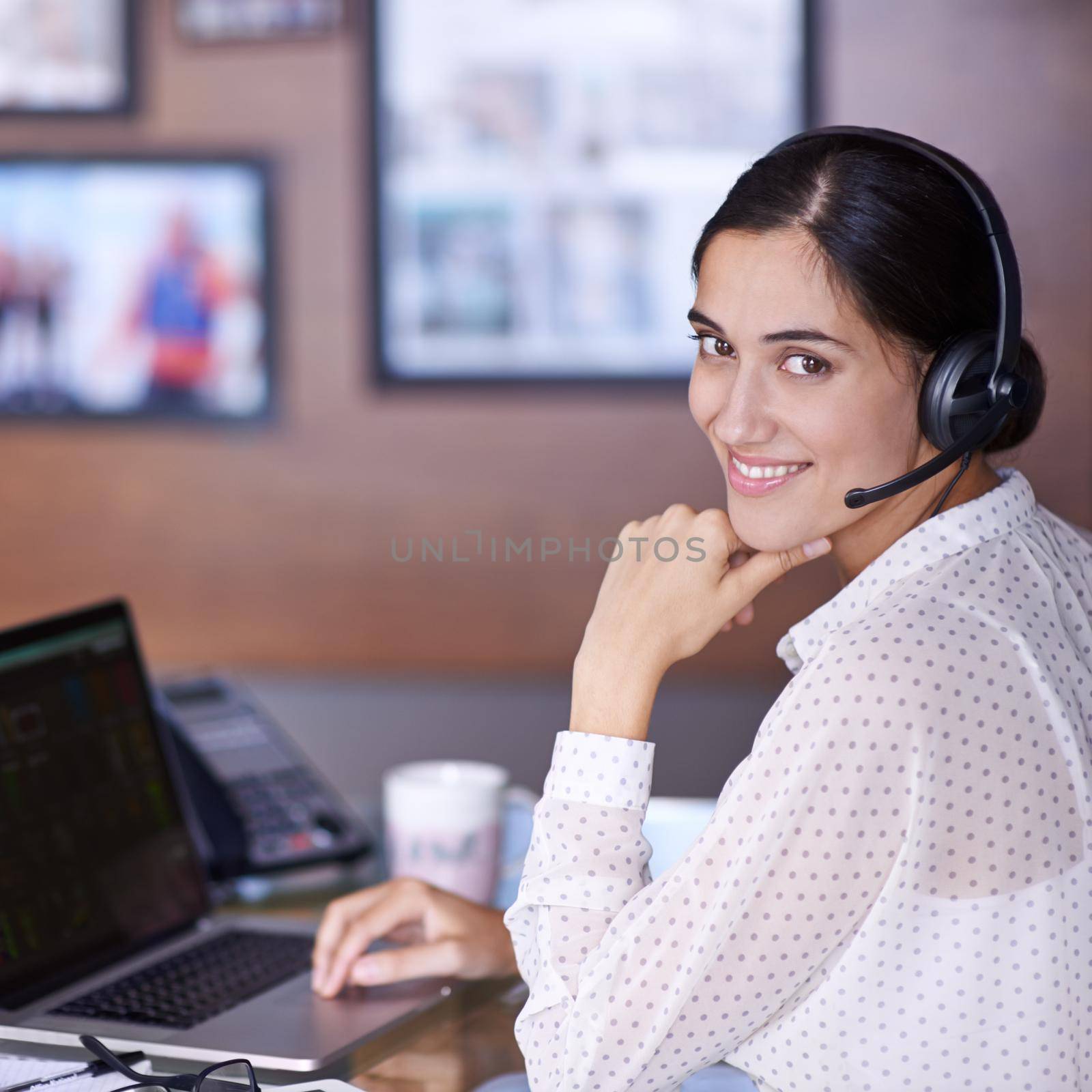 Waiting to help you out. an attractive young businesswoman working on a laptop while wearing a headset. by YuriArcurs