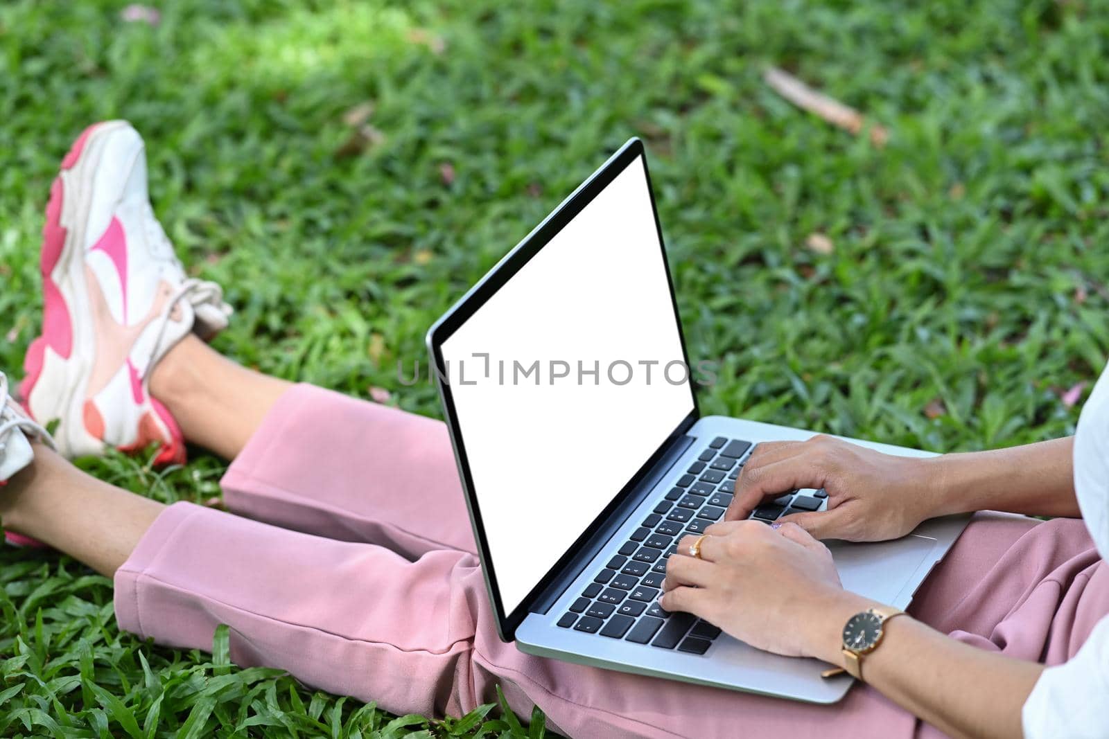 Cropped shot young woman sitting on grass in the park and working with computer laptop. by prathanchorruangsak