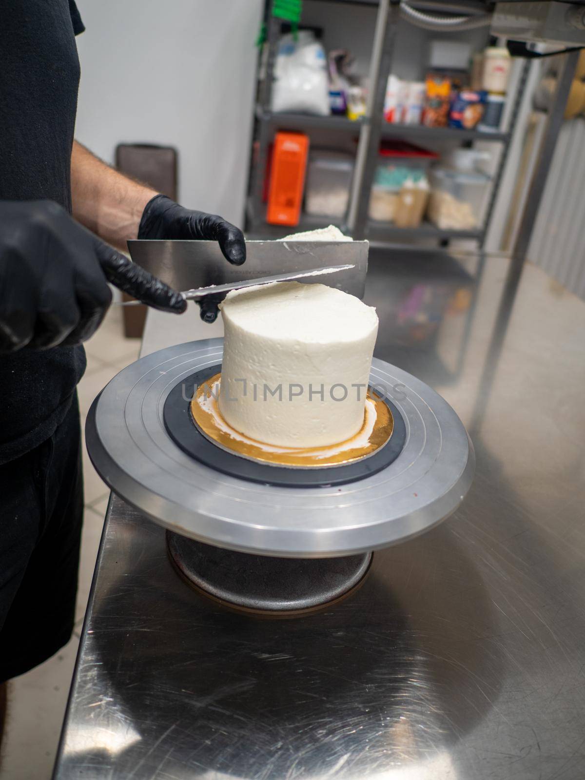 Decorator using spatula and scraper to smooth buttercream on a frosted cake
