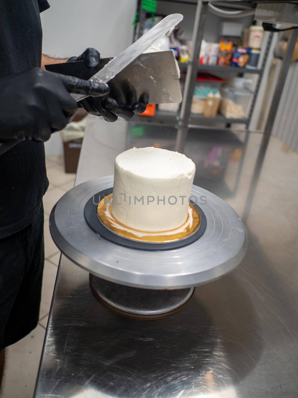 Decorator using spatula and scraper to smooth buttercream on a frosted cake