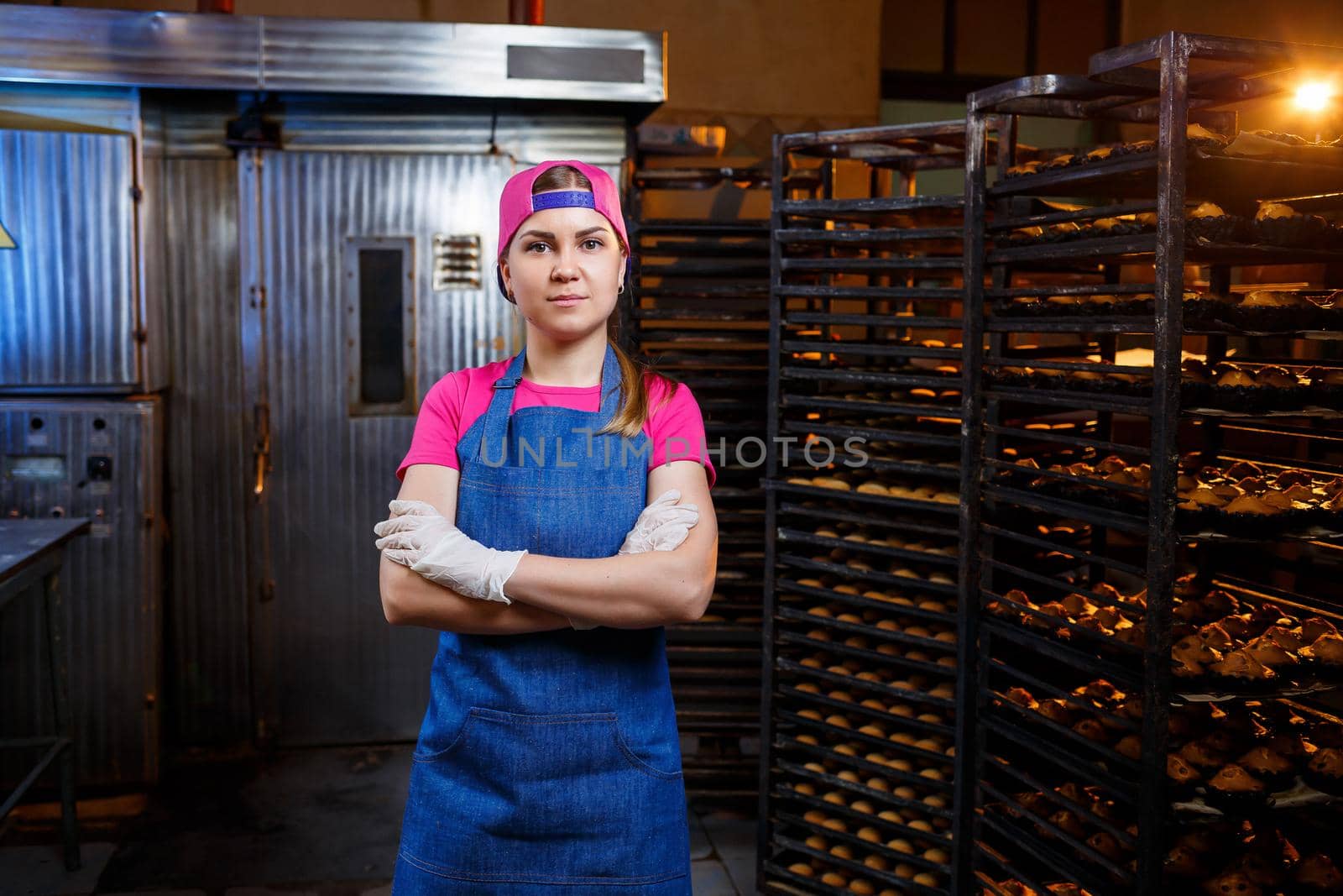 A professional baker girl is standing near shelving with trays of fresh biscuits. Sweet pastries in a bakery