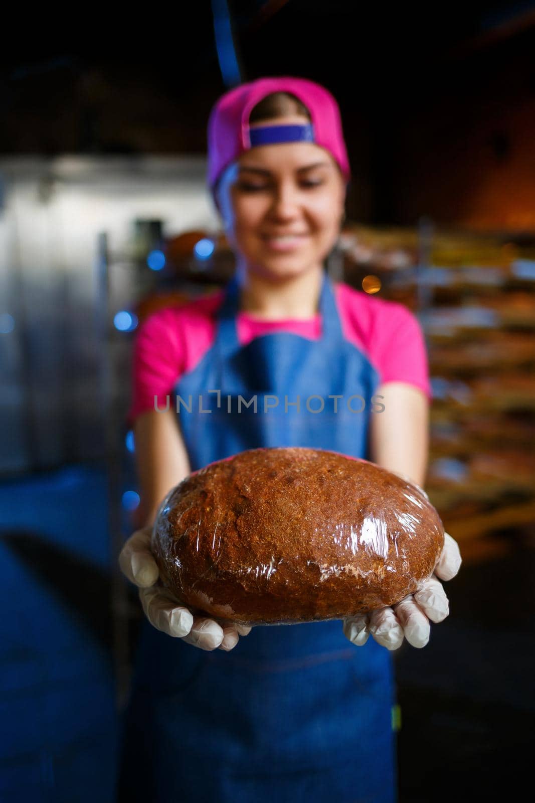 A baker girl takes hot bread in a bakery against the background of shelving with bread. Industrial production of bread. The stage of baking in a bakery