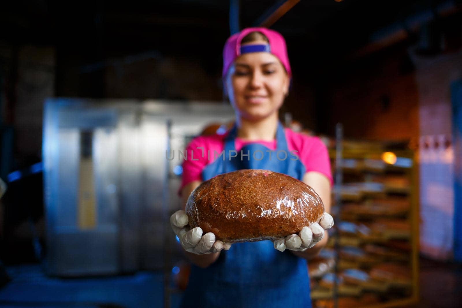 Girl baker takes hot bread in the bakery on the background of the rack. Industrial production of bread. Baking stage in the bakery