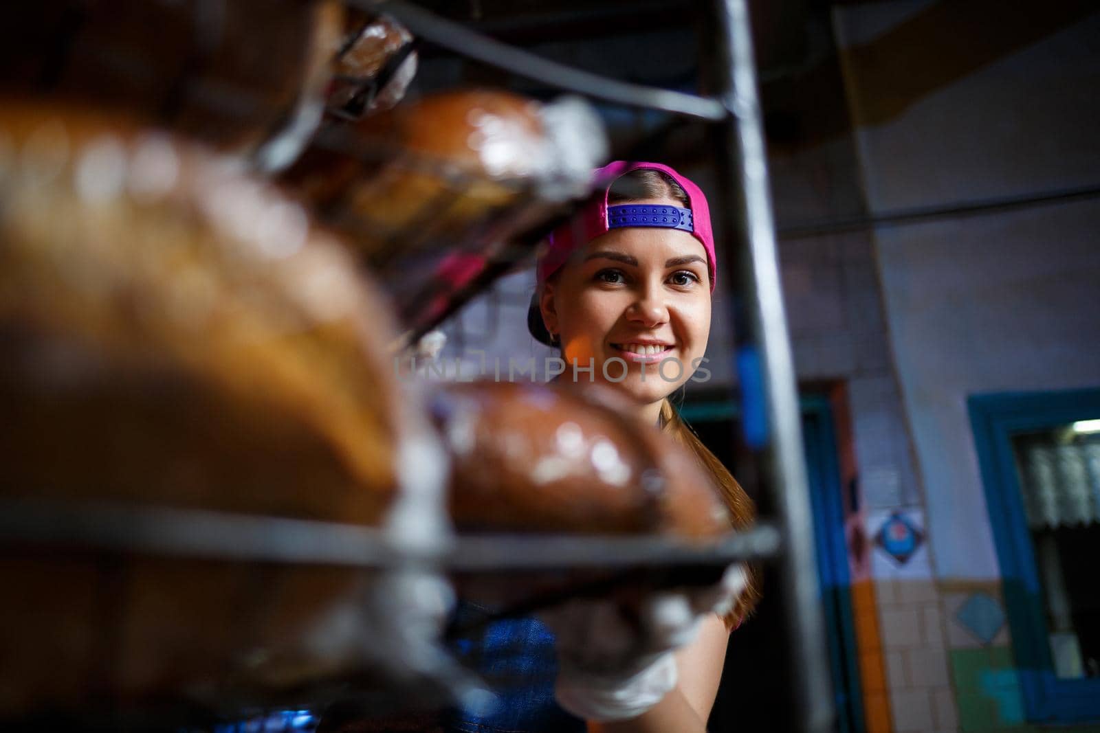 A young girl works in a bakery. She puts bread on a shelf. Woman baker at workplace in a bakery. A professional baker holds bread in his hands. Bread production concept
