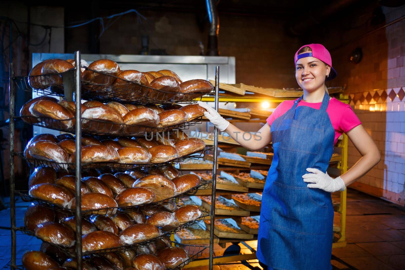 A young girl works in a bakery. She puts bread on a shelf. Woman baker at workplace in a bakery. A professional baker holds bread in his hands. Bread production concept