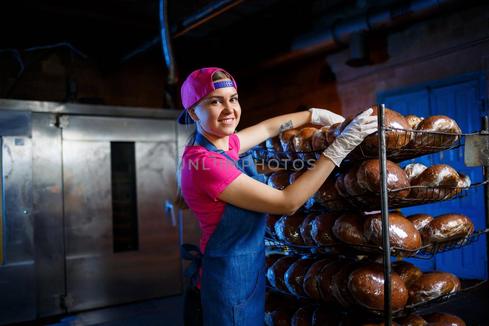 Professional baker - a young pretty woman in a denim apron holds fresh bread in her hands. Bakery products. Bread production