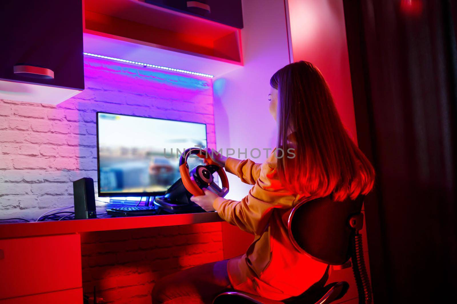 girl gamer playing racing on a computer. She uses a steering wheel. emotional play