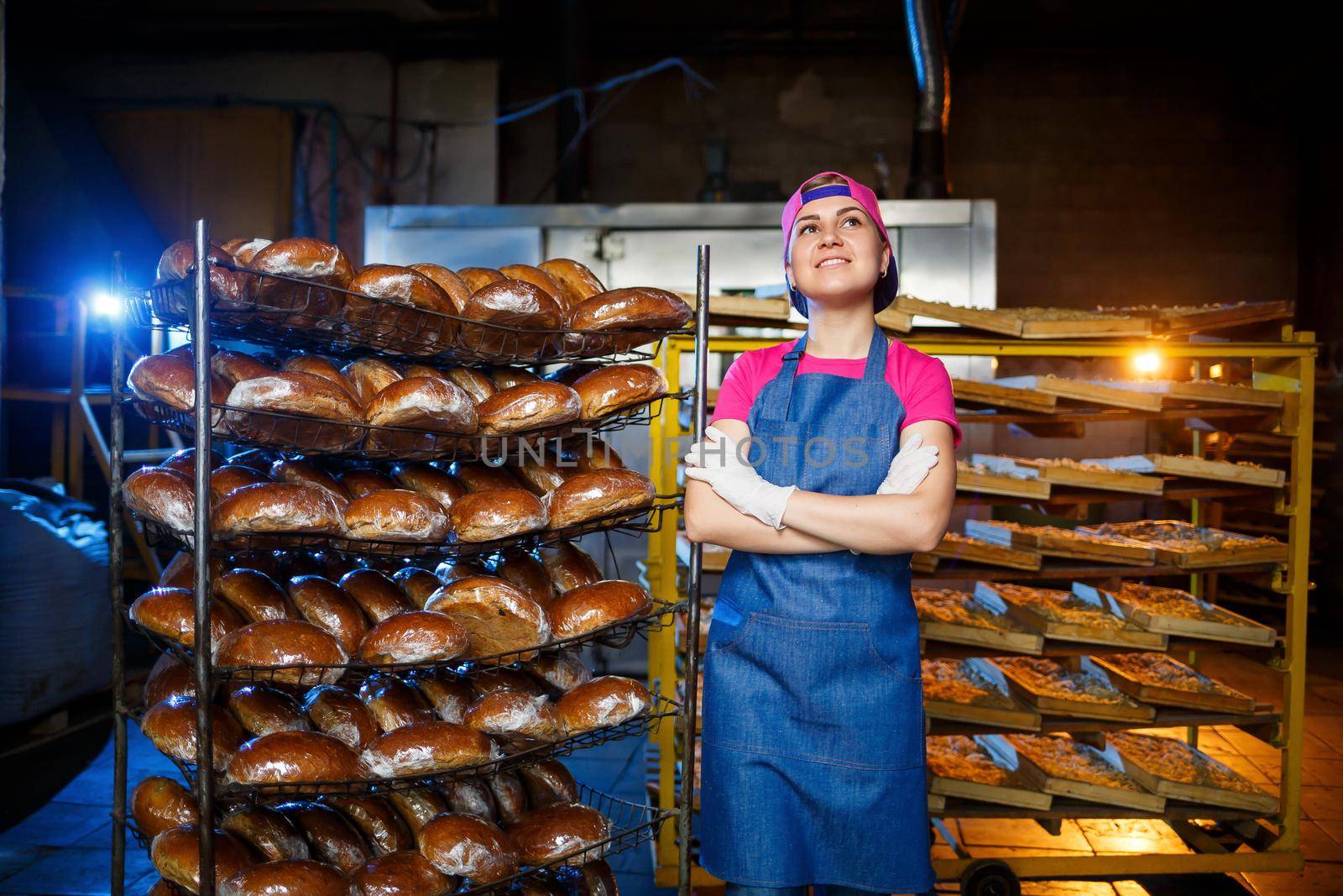 Portrait of a baker girl against the background of shelves with fresh bread in a bakery. Industrial bread production