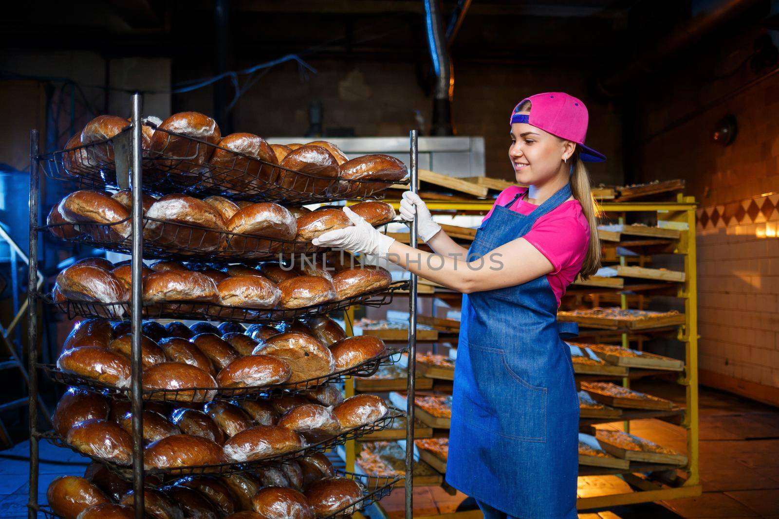Professional baker - a young pretty woman in a denim apron holds fresh bread in her hands. Bakery products. Bread production