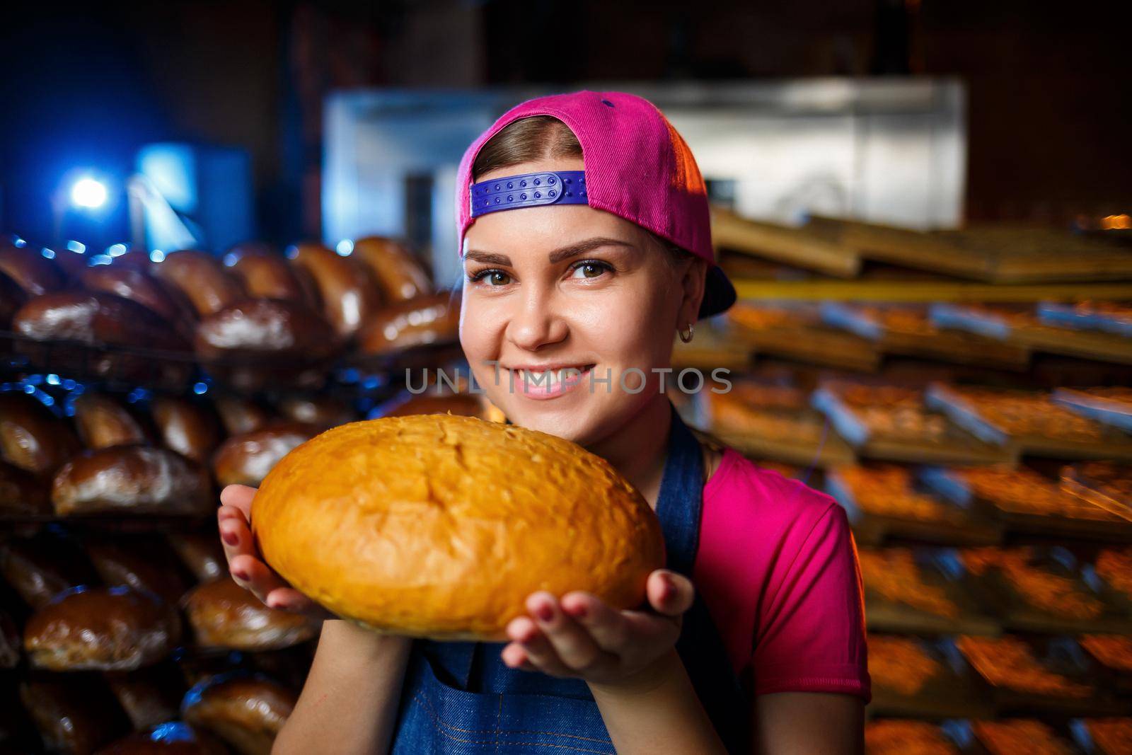 Portrait of a baker girl with bread in her hands on the background of shelves in a bakery. Baker's hands with bread. Industrial production of bread