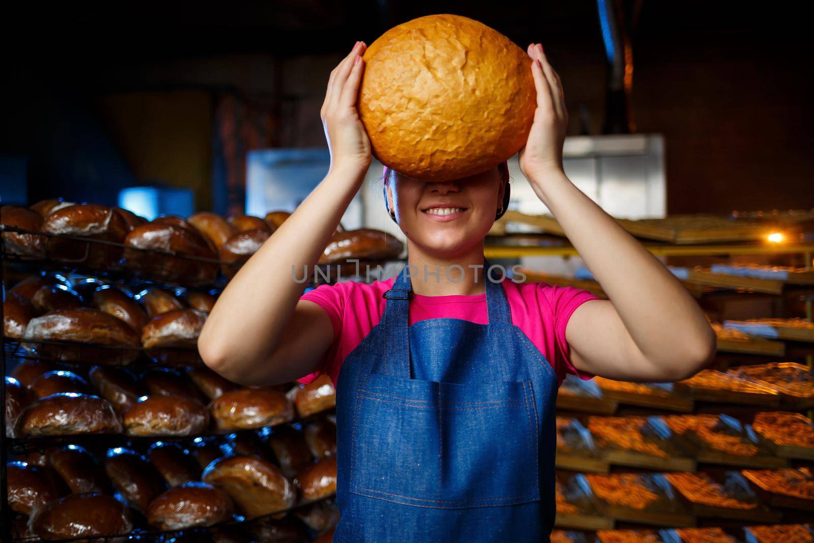 The stage of baking in a bakery. Portrait of a baker girl with bread in her hands against the background of shelving in a bakery. Hands of a baker with bread. Industrial bread production